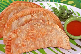 close up view of Empanadas (Beef Turnovers) and sauce on the side, served with fresh herbs