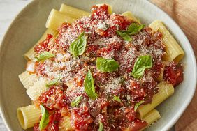 looking down at a bowl of rigatoni noodles topped with arrabbiata sauce garnished with cheese and fresh basil 