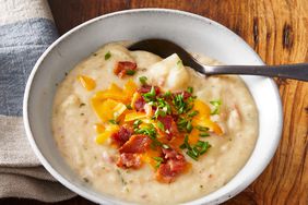 a close up view of a single serving of creamy bowl of absolutely ultimate potato soup topped with crispy bacon bits, cheese, and green onion