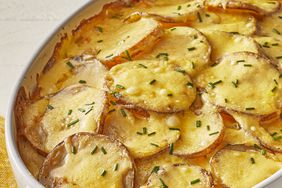 a close up view of creamy au gratin potatoes in a white oval casserole dish topped with fresh chives