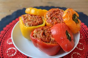 a close up view of an orange, yellow, and red stuffed bell peppers on a single plate.