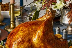 a low angle view of a perfectly golden-brown, whole turkey sitting on a dressed dining room table.