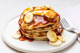 a low angle view looking into a delicious stack of banana pancakes garnished with fresh sliced bananas, syrup, and melting butter