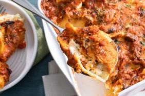 close up view of a stuffed shell in a serving spoon and stuffed shells in a baking dish