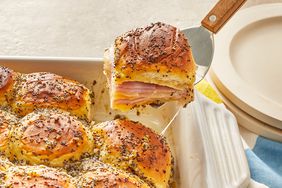 a ham and cheese slider being lifted from a white casserole dish of freshly baked sliders. 