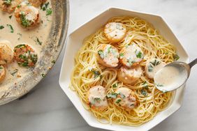 overhead view of scallops over spaghetti in a large white bowl, with sauce spooned over pasta.