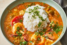 a close up view of a single bowl of creole gumbo served with steamed white rice and fresh herbs