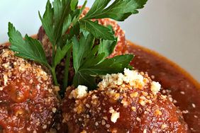 high view of Italian meatballs served with sauce over top with a sprinkle of parmesan cheese and garnished with Italian parlsey