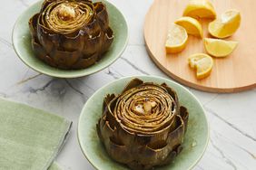 looking at two roasted artichokes in small bowls and lemon on a cutting board 
