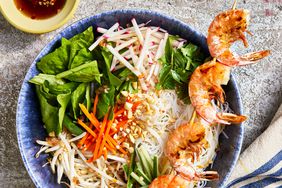looking down at vermicelli noodle bowl with shrimp on a skewer, vegetables and peanuts