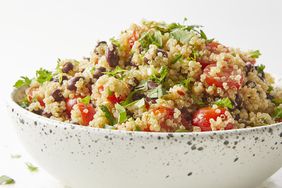 mid angle, looking at a heaping bowl of quinoa salad with tomatoes, olives and fresh herbs 
