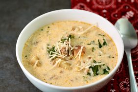 sausage, potato, and kale soup in white bowl topped with cheese