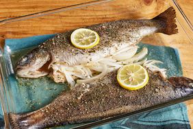 high angle looking at two rainbow trout garnished with lemon slices and stuffed with onions, in a baking dish