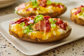 a low angle, close-up view looking into multiple ultimate twice baked potatoes topped with crispy bacon and sliced green onions. 