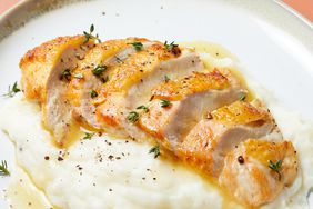 close up on a pan roasted chicken breast, sliced, and resting on a serving of mashed potatoes