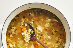 close up view of chicken noodle soup in a pot with a wooden spoon