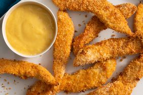 a close up, top down view of a plate of golden-brown baked chicken tenders served with a side of honey mustard.
