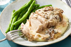 Close up on a plate of mashed potatoes, topped with baked pork chops with cream of mushroom soup, and a side of green beans.