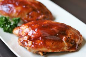 a close up view of an oven baked bbq chicken thigh on a white plate. 