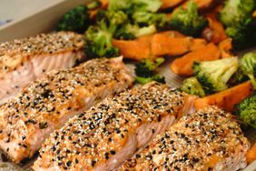 four salmon fillets topped with "everything bagel" seasoning on a sheet pan with broccoli florets and sweet potato wedges