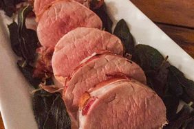 close up view of a sliced Prosciutto-Wrapped Pork Tenderloin with Crispy Sage on a white platter