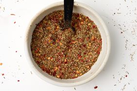 Italian seasoning in a white bowl with a teaspoon resting inside. 