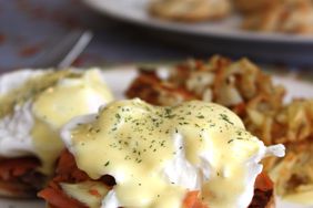 close up view of smoked salmon eggs Benedict topped with Blender Hollandaise Sauce, with potato hash in the background on a plate