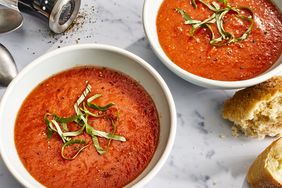 close up view of two bowls with Fresh Tomato Soup garnished with fresh basil, next to bread 
