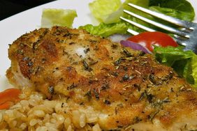 close up view of baked chicken on a plate with brown rice and salad