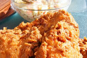 close up view of triple-dipped fried chicken, with coleslaw in a bowl behind the chicken