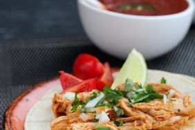 close up view of Instant Pot Salsa Chicken on top of a tortilla, garnished with tomatoes, limes, onions and fresh herbs on a plate