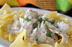 closeup of a serving of creamy-looking chicken stroganoff over egg noodles, garnished with chopped parsley
