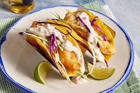 high angle looking down at two fish tacos garnished with lime wedges