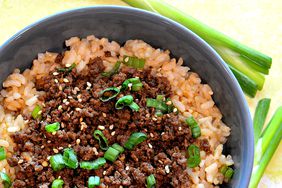 A bowl of seasoned ground beef on brown rice garnished with green onion