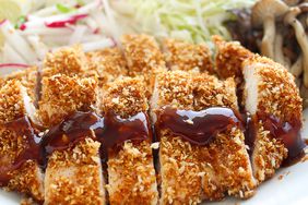 closeup of a fried chicken cutlet on a plate, sliced and drizzled with tonkatsu sauce