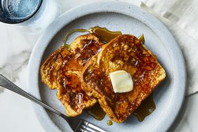 a close up, overhead view of two slices of golden-brown french toast plated and topped with melting butter and syrup