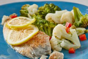 low angle looking at tilapia topped with lemon slices and served with broccoli, cauliflower and peppers on a blue plate 