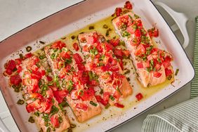 overhead view of four salmon fillets in a casserole dish, topped with chopped tomatoes and green onions