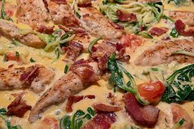 chicken in skillet with cream sauce, spinach, tomatoes, and bacon