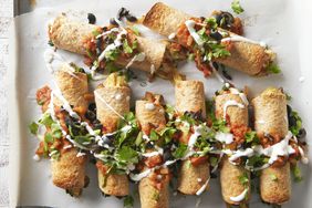  Baked breakfast taquitos on baking sheet topped with tomatoes, cilantro and crema