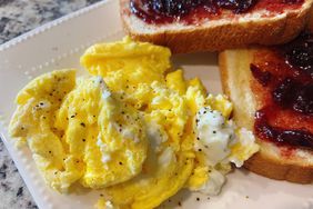 Scrambled eggs on white plate with toast and jam