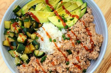 white bowl with rice, salmon, cucumbers, and avocado, with sriracha drizzle