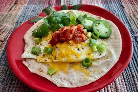 beautifully fried egg on tortilla with salsa, cheese, jalapenos, and cilantro on red plate