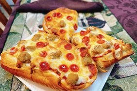 Baguette pizza with salami and meat on white plate set on green tablecloth
