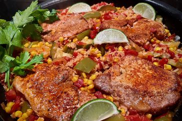 seasoned pork chops in skillet with rice, corn, tomatoes, and lime slices