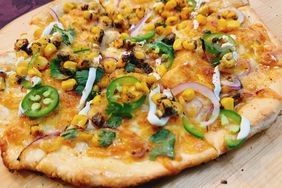 grilled pizza on board with jalapeno slices, red onion, corn, cilantro and crema