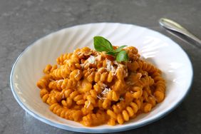 white bowl of curly pasta with light red Trapanese sauce and basil sprig