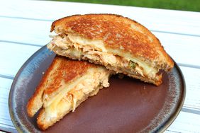 halved golden brown chicken melt sandwich on a dark russet plate on outdoor table