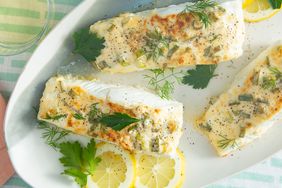 overhead view cropped into a plate of a few halibut filets garnished with fresh herbs and lemon slices