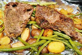 foil lined sheet pan with cooked steak, halved baby potatoes, and whole green beans